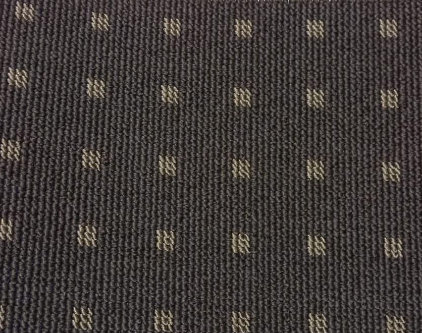 Zbliżenie na ciemnoszarą wykładzinę dywanową z regularnym wzorem małych, beżowych kwadratów ułożonych w rzędach.