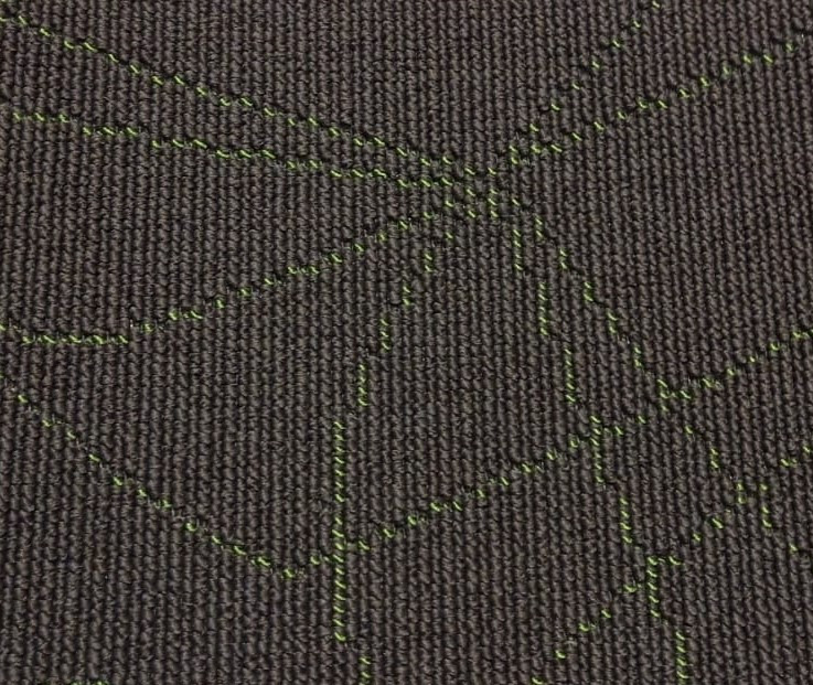 Zbliżenie na szarą wykładzinę dywanową z geometrycznym wzorem w postaci jasnych, zielonych przeszyć.