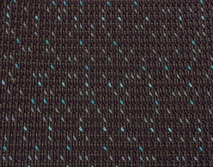 Zbliżenie brązowej wykładziny dywanowej z regularnym wzorem turkusowych i szarych kropek.
