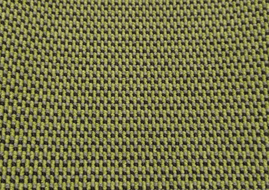 Tekstura wykładziny w odcieniach zieleni, szarości i czerni, tworząca geometryczny wzór. Widoczna z bliska, prezentuje detale splotu.