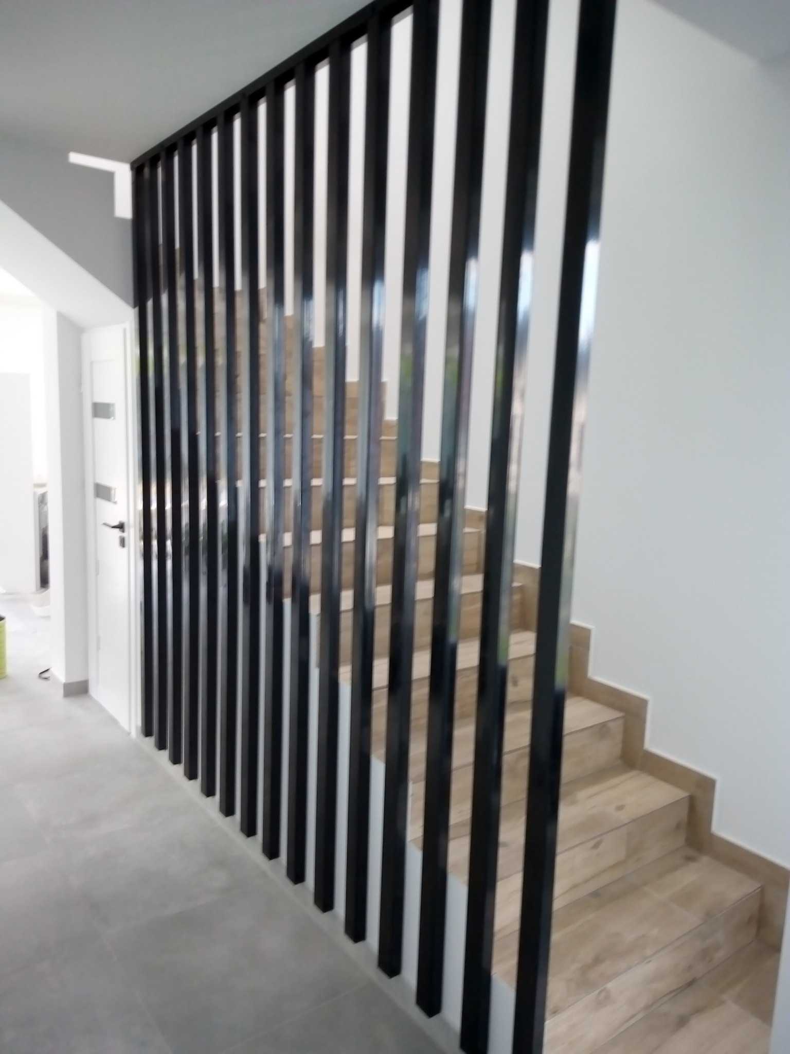 Schody wyłożone płytkami imitującymi drewno, oddzielone od korytarza czarnymi, pionowymi listwami.