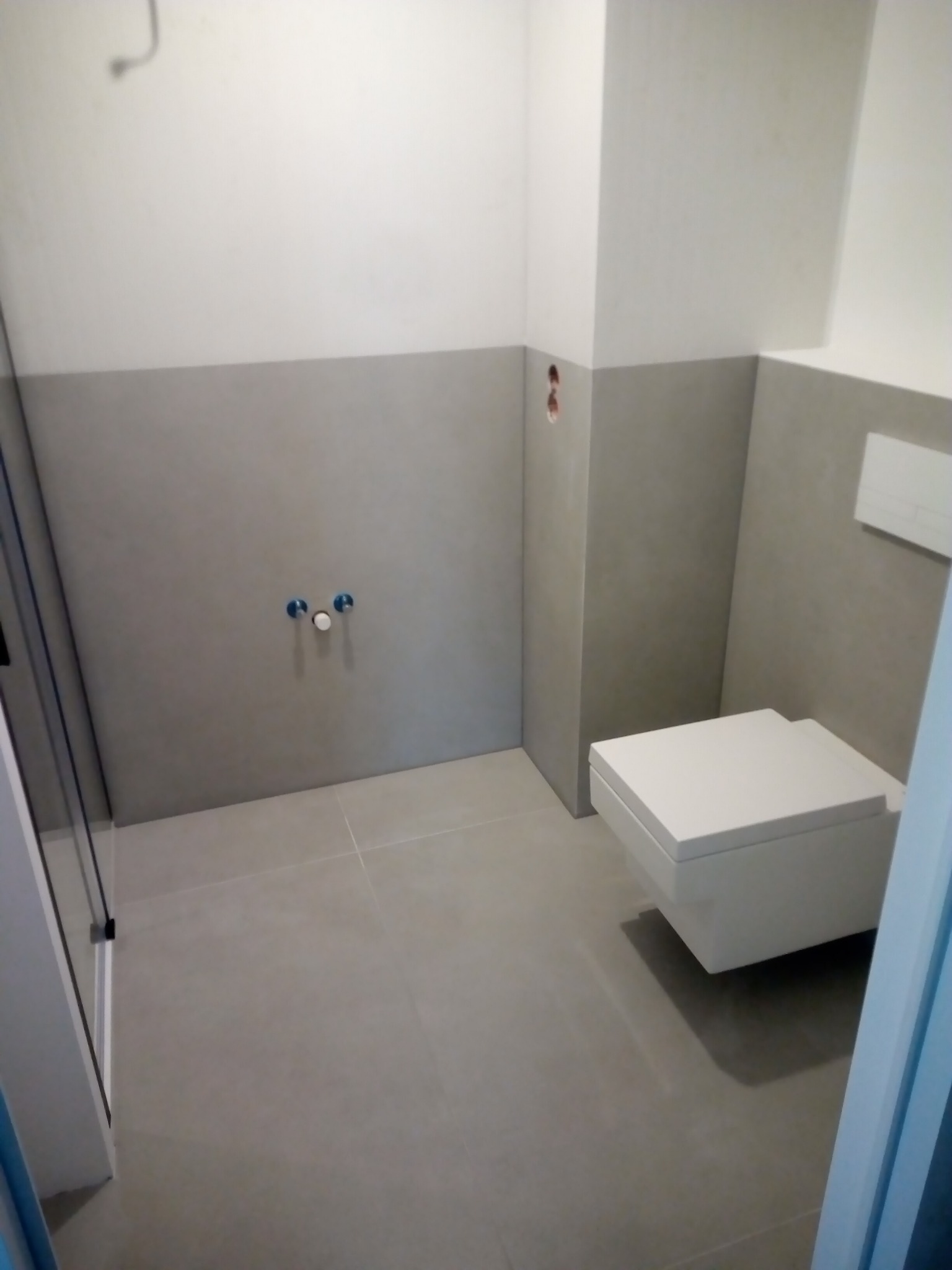 Szara łazienka w trakcie wykańczania w Krakowie: widoczne przygotowane ściany pod glazurę, zamontowana podwieszana toaleta oraz instalacja prysznicowa.