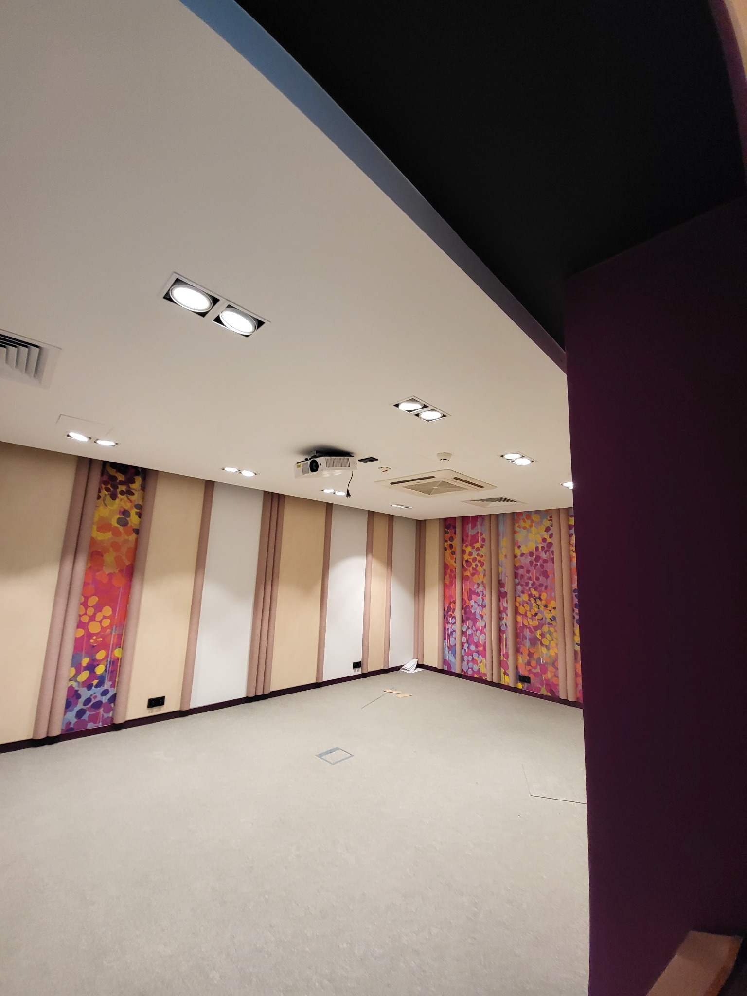 Wnętrze pustego pomieszczenia z projektorem sufitowym, wbudowanymi lampami LED i dekoracyjnymi panelami ściennymi w odcieniach beżu, bieli i różu z motywem kwiatowym.