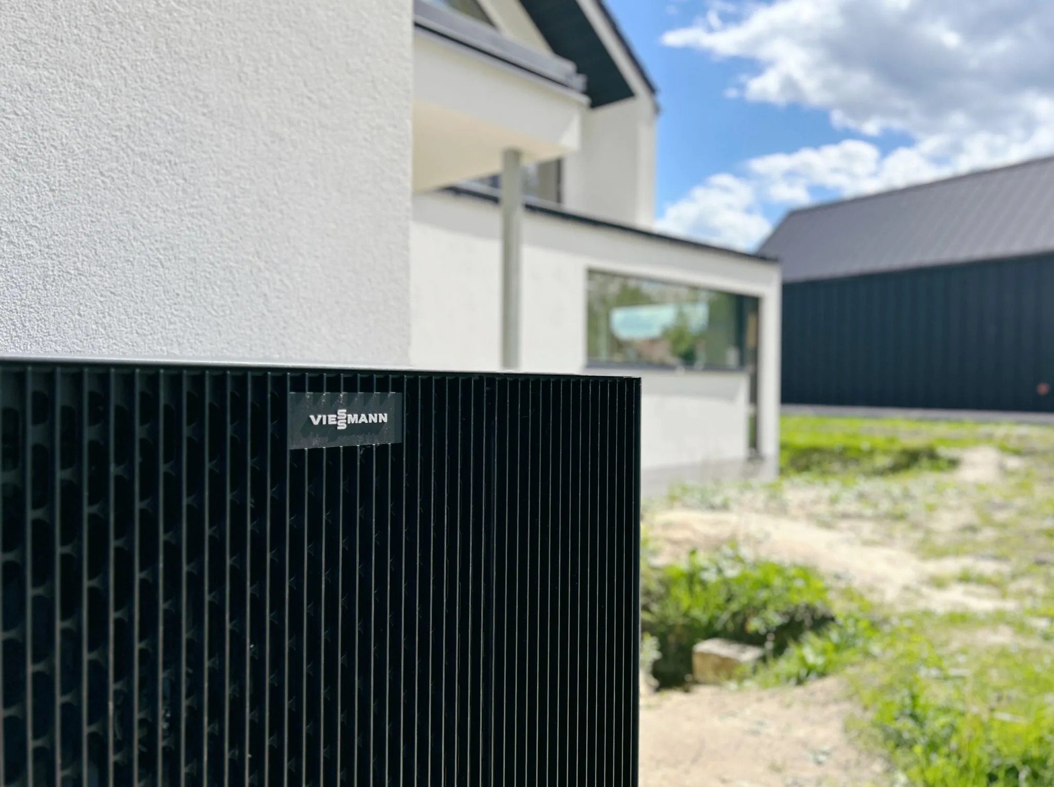 Czarna pompa ciepła Viessmann na tle białego domu z płaskim dachem i zielenią ogrodu.