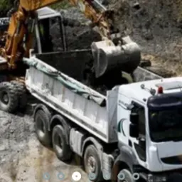 Żółta koparka kołowa ładuje ziemię do białej ciężarówki na terenie budowy.