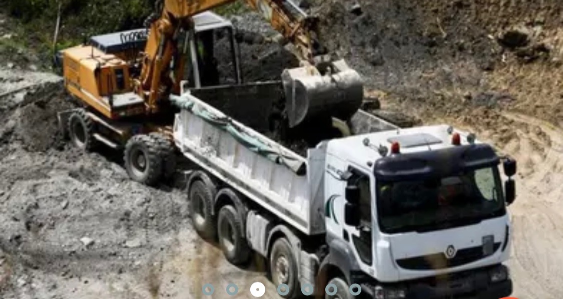 Żółta koparka kołowa ładuje ziemię do białej ciężarówki na terenie budowy.