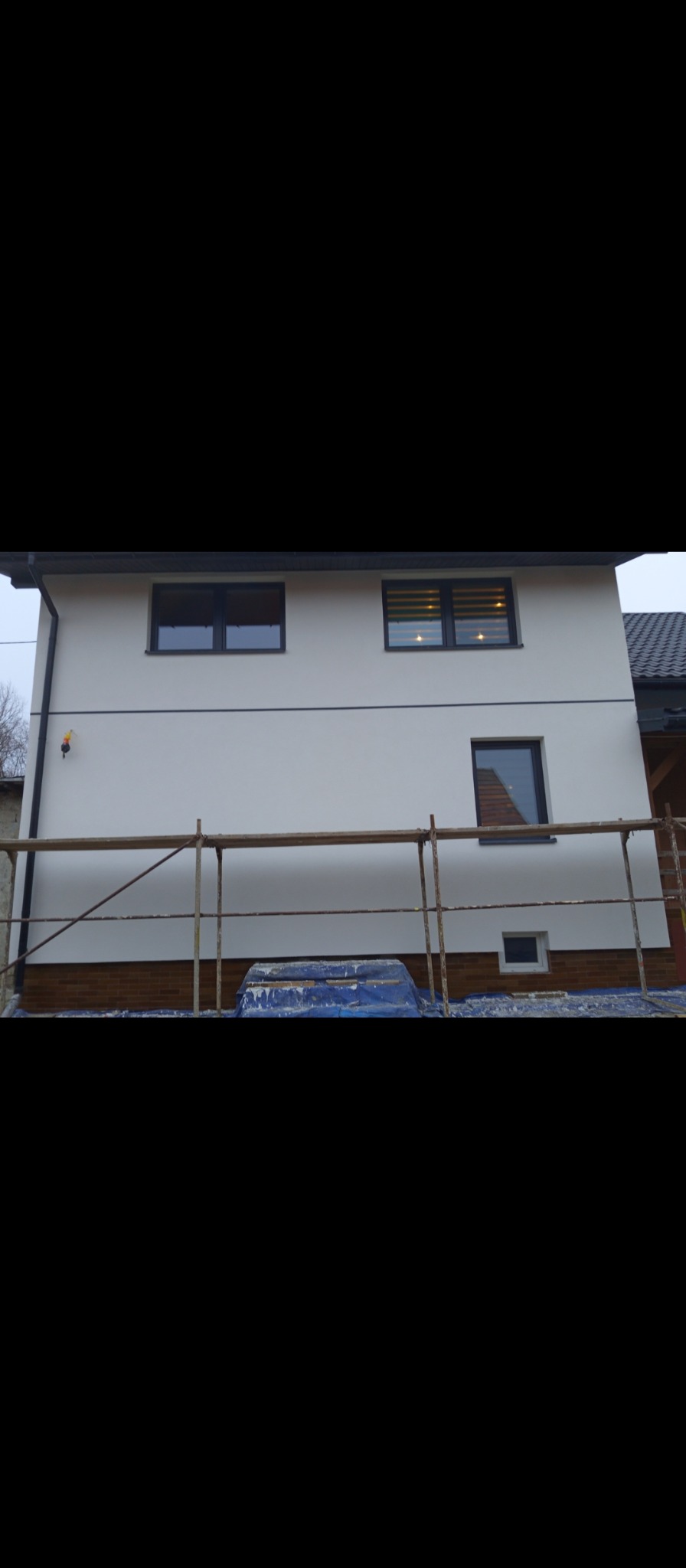 Boczny widok domu z nową, białą elewacją i rusztowaniem w trakcie prac wykończeniowych.