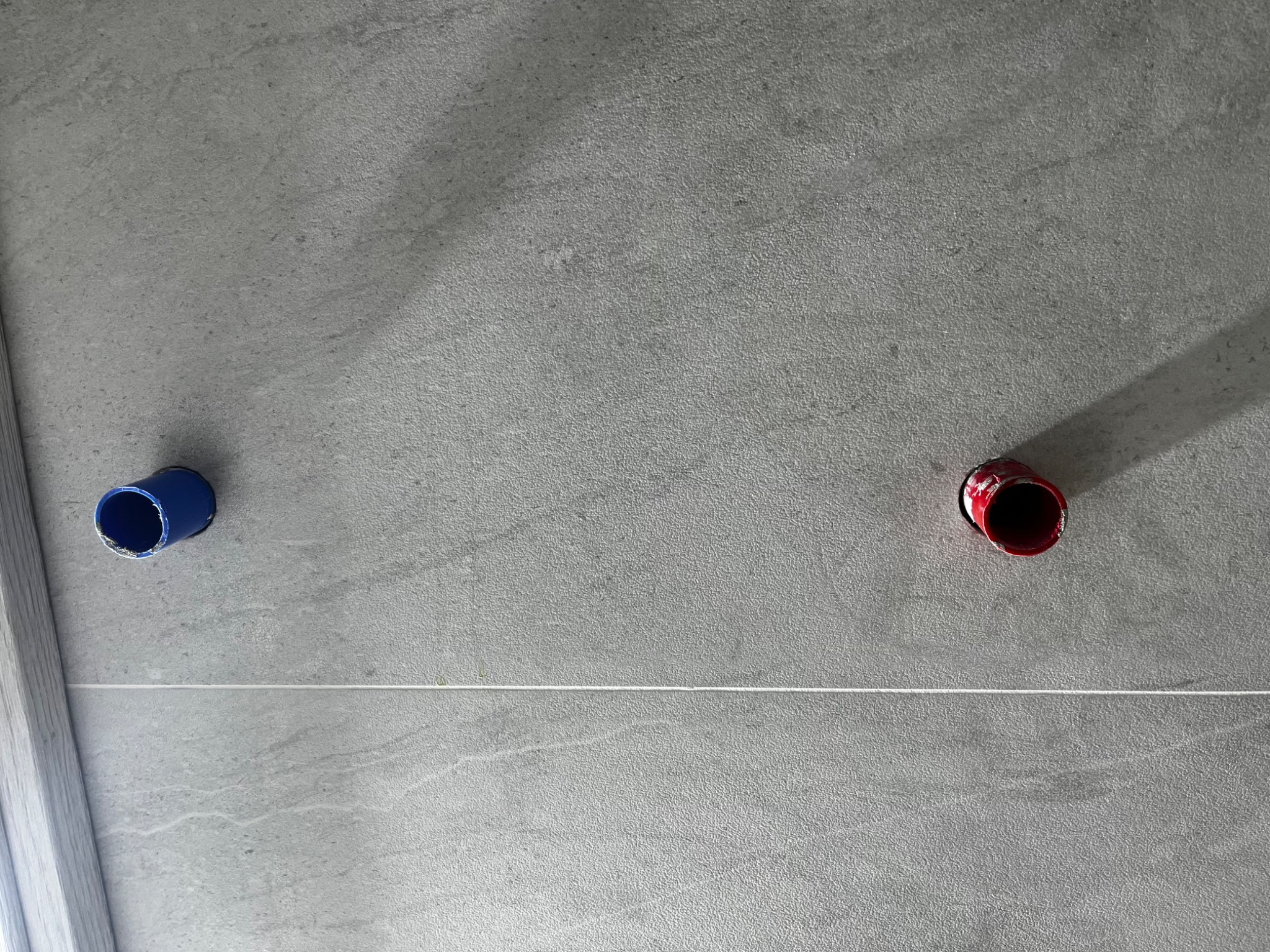 Szara ściana wyłożona płytkami imitującymi kamień, z widocznymi otworami na rury w kolorze niebieskim i czerwonym, wyznaczonym poziomem laserowym.