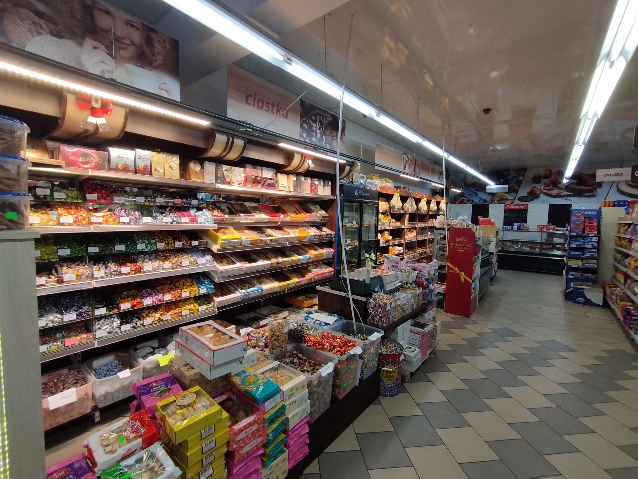 Półki sklepowe wypełnione różnorodnymi słodyczami i ciastkami w opakowaniach, widok z perspektywy alejki w sklepie spożywczym.