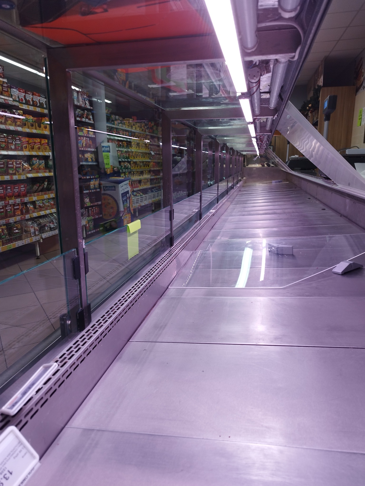 Długi rząd lamp fluorescencyjnych zamontowanych nad szklaną witryną chłodniczą w supermarkecie, widok z dołu.