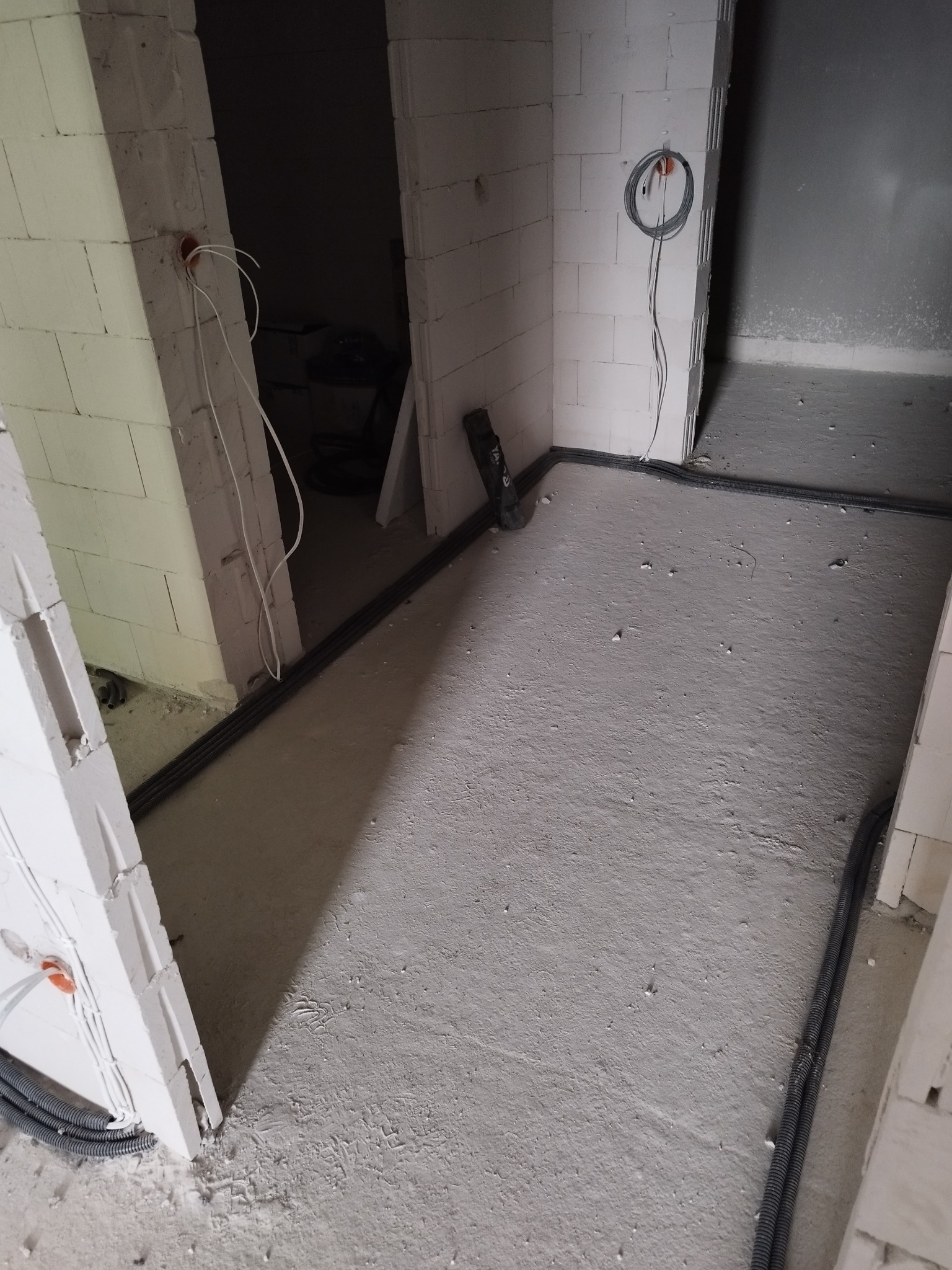 Wnętrze w trakcie instalacji elektrycznej: kable w peszlach ułożone wzdłuż ścian, wystające przewody ze ścian z pustaków.