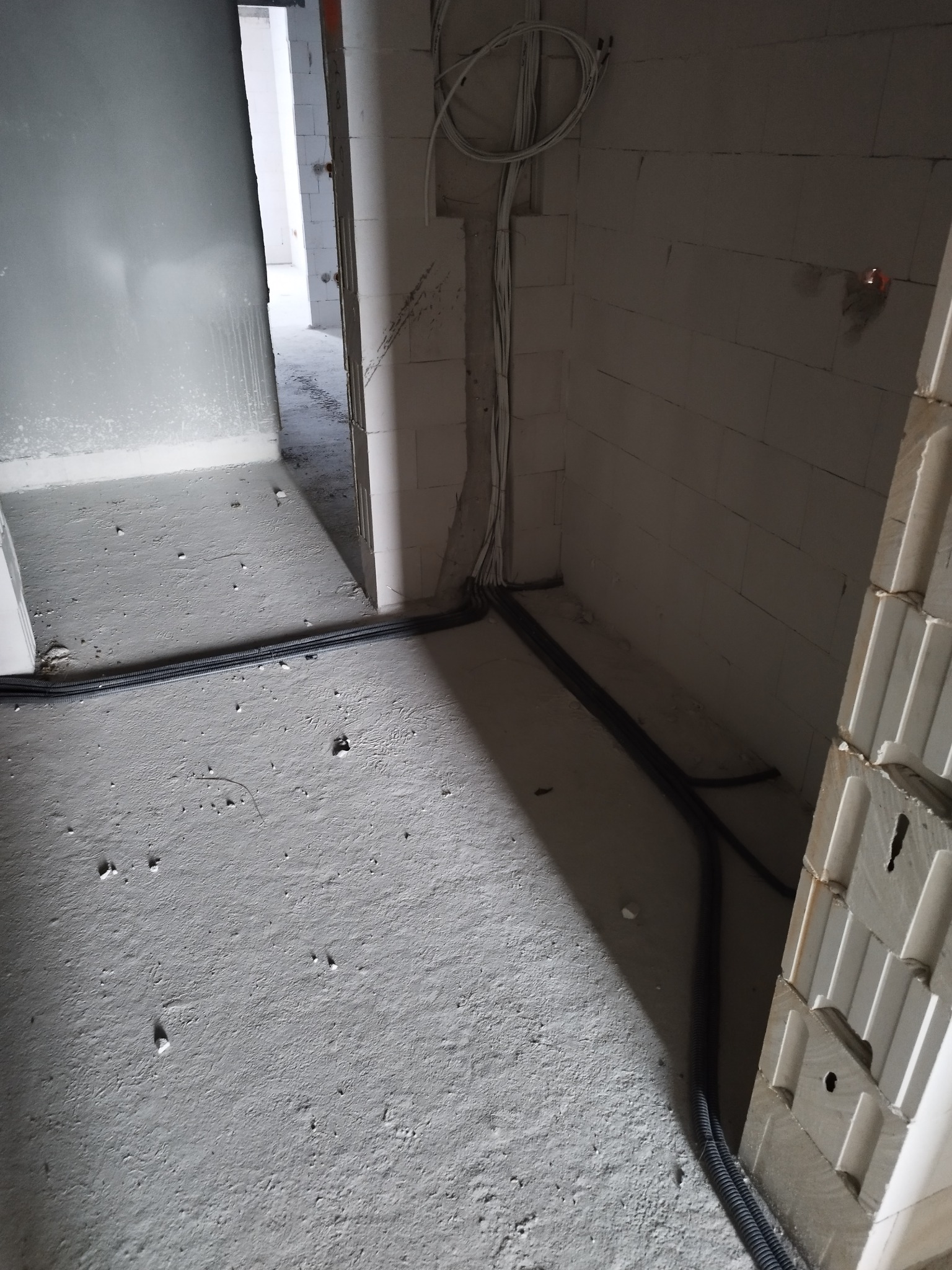 Surowy stan wnętrza w trakcie prac instalacyjnych: przewody elektryczne w peszlach ułożone wzdłuż ściany z betonu komórkowego, widoczne wystające kable ze ściany. Pomieszczenie w stanie...