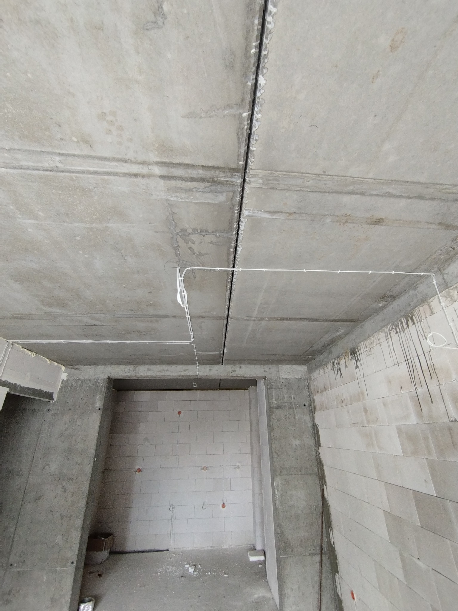 Kable elektryczne prowadzone po suficie w surowym stanie budynku w Krobii, widoczne ślady po wierceniu i montażu.