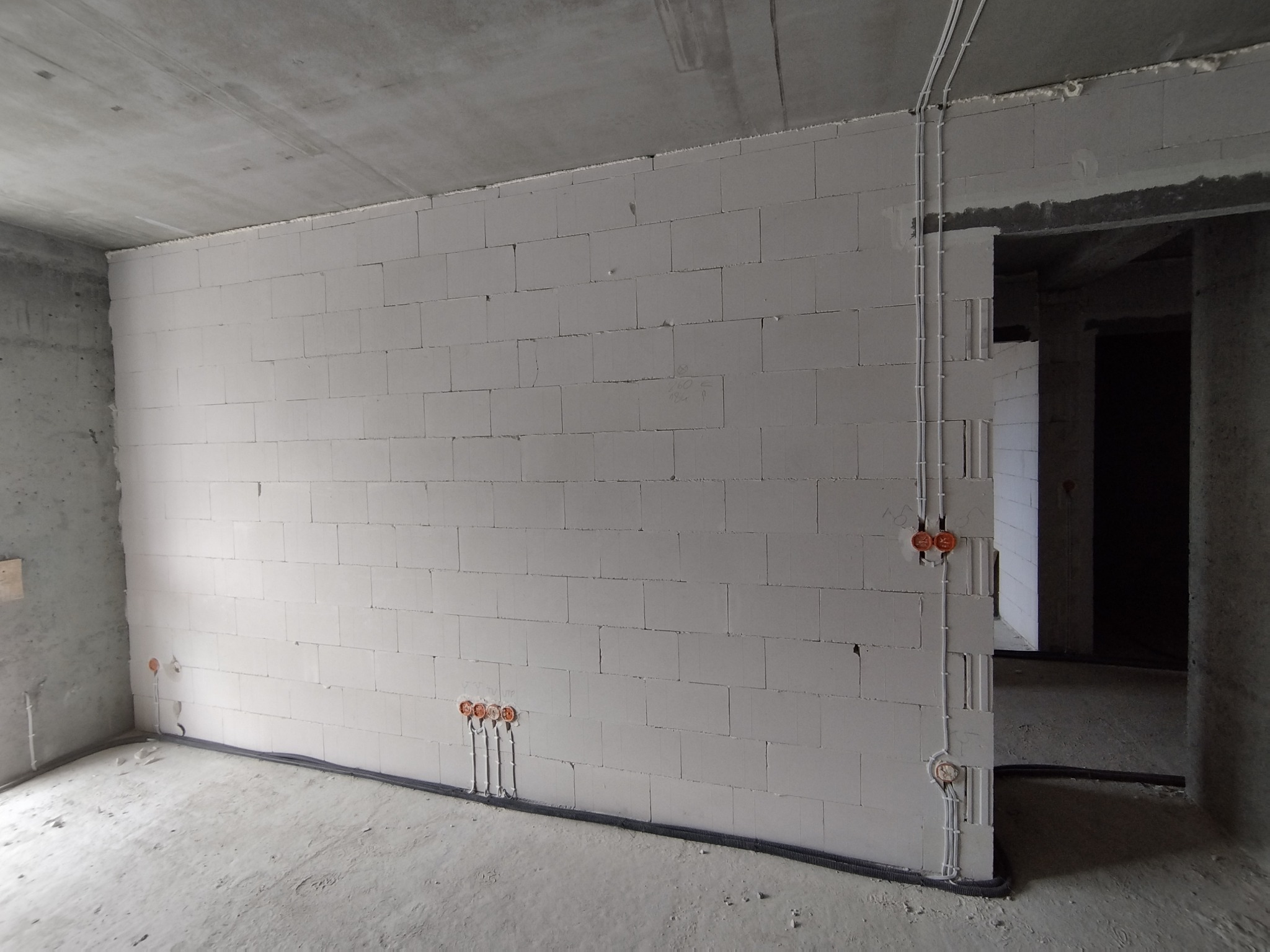 Wnętrze surowego budynku z widoczną instalacją elektryczną w ścianie z betonu komórkowego, kable w peszlu ułożone wzdłuż ściany i pionowo do gniazdek.