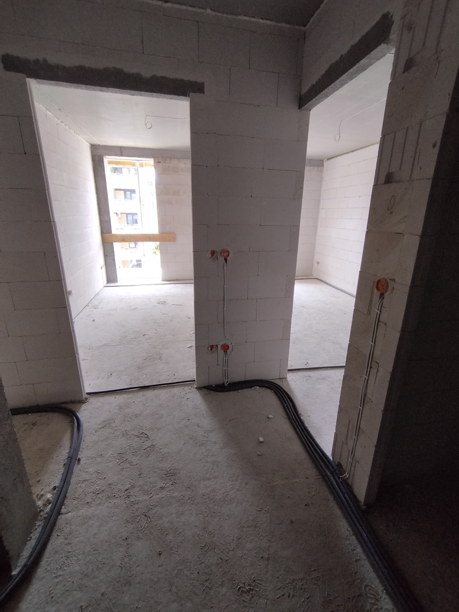 Surowy stan mieszkania w bloku: widoczne kable elektryczne w peszlach prowadzone po podłodze i wyprowadzone gniazdka w ścianach z betonu komórkowego.