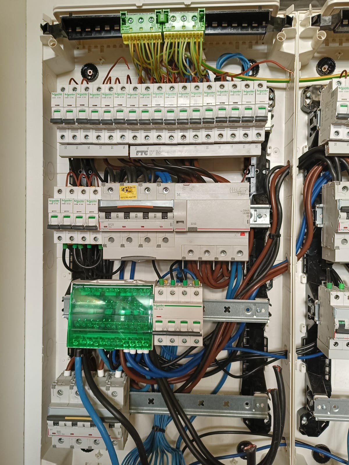 Otwarta skrzynka rozdzielcza z zainstalowanymi bezpiecznikami i przewodami w różnych kolorach, widoczne elementy marki Schneider Electric i Hager.