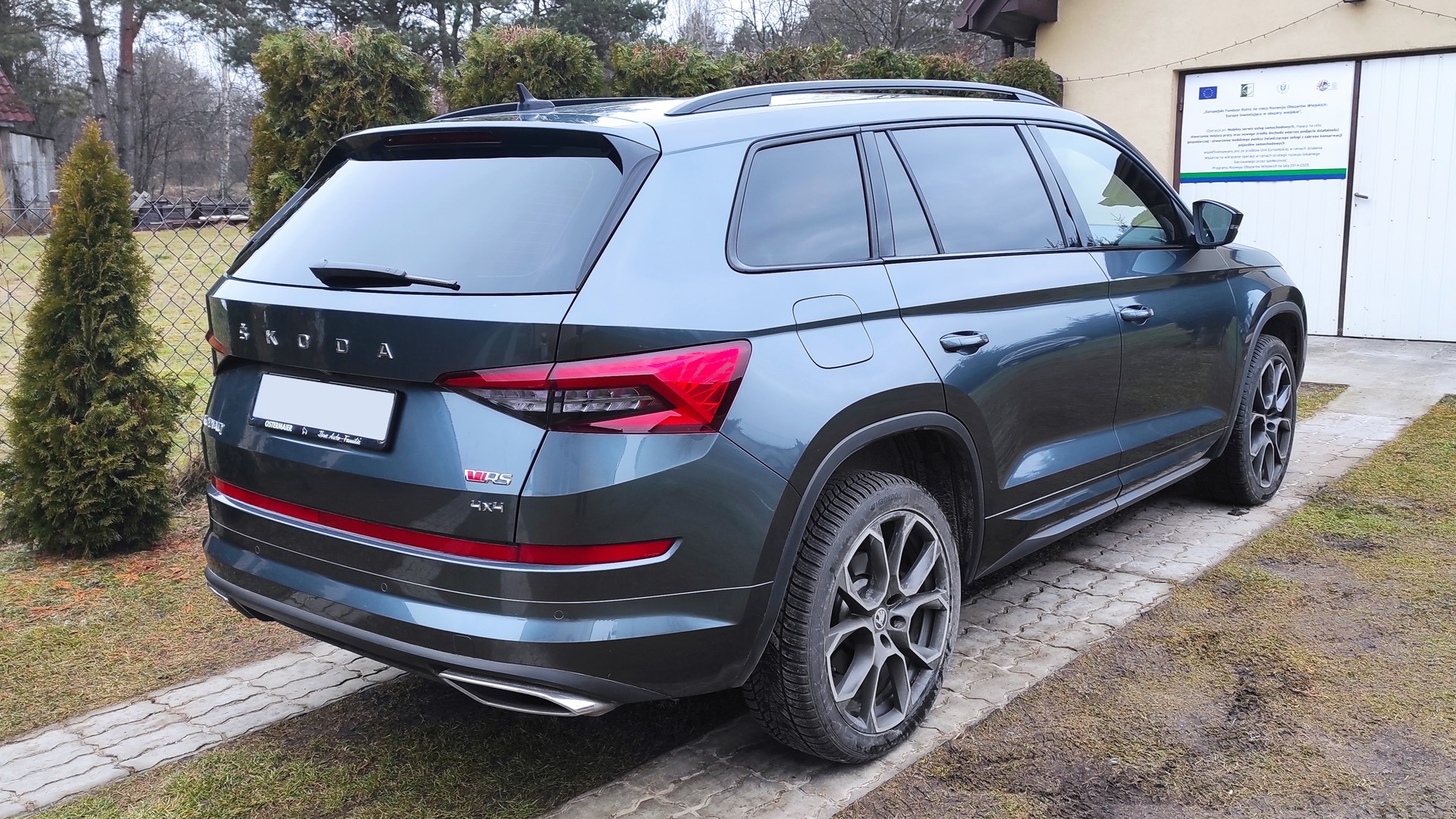 Ciemnoszara Skoda Kodiaq VRS z mocno przyciemnionymi tylnymi szybami, zaparkowana na podjeździe z kostki.