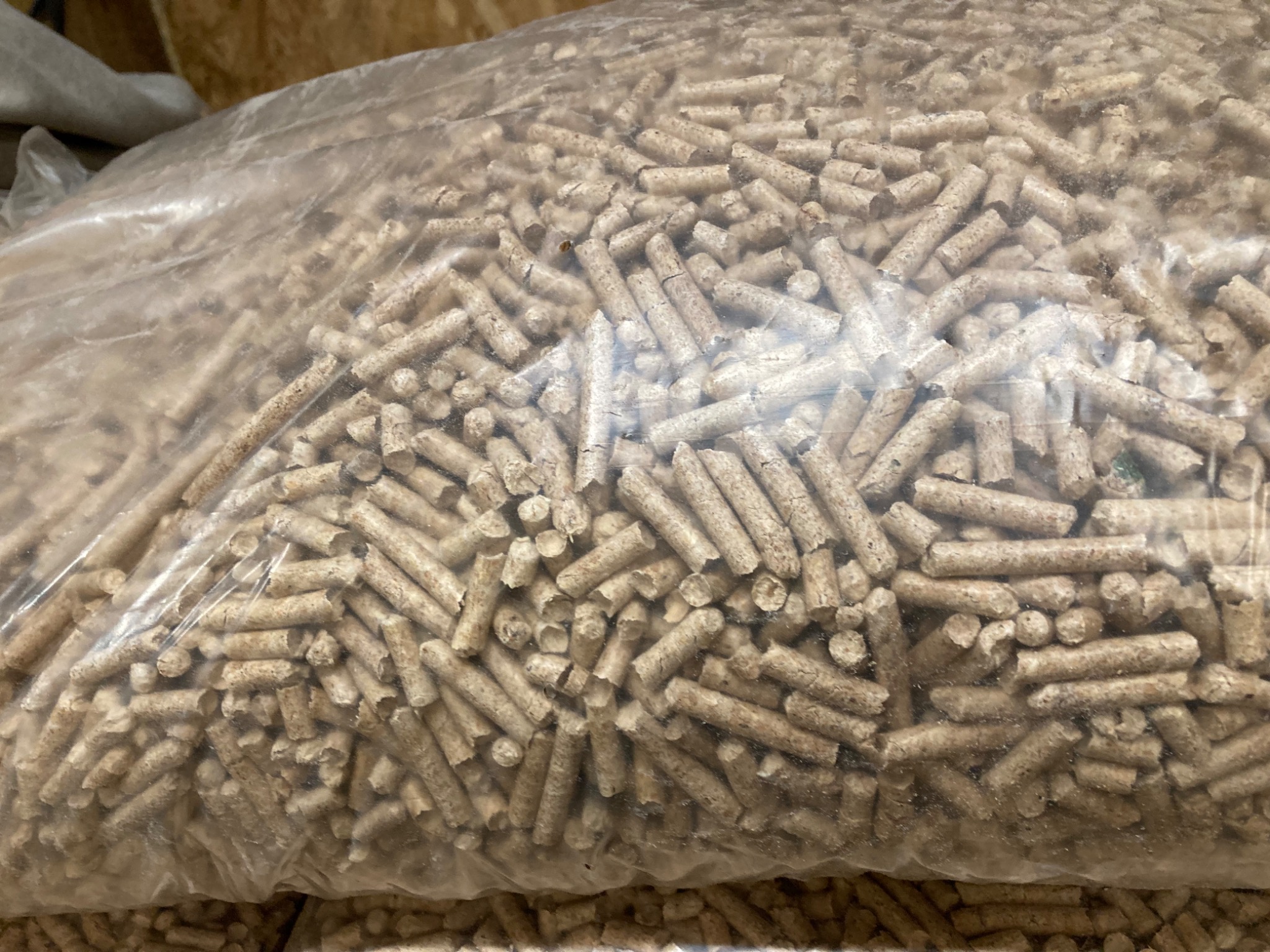 Wypełniony worek przezroczystego tworzywa z jasnymi, cylindrycznymi brykietami drzewnymi, widoczne drobne pęknięcia na powierzchni niektórych pelletów.
