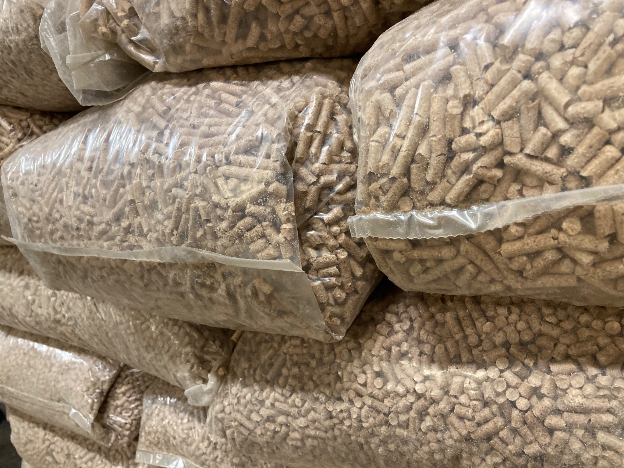 Stos worków z pelletem drzewnym, widoczne detale struktury pelletu przez przezroczyste opakowanie, ułożone warstwami w magazynie.