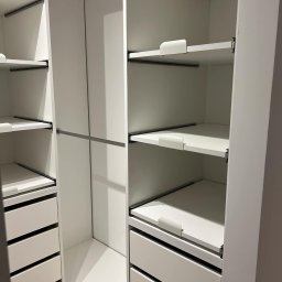Face Front Konrad Olborski - Wnętrze białej garderoby z szufladami i półkami, widoczne drążki na ubrania i systemy mocowania półek.