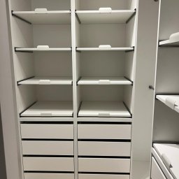 Face Front Konrad Olborski - Wnętrze białej szafy wnękowej z szufladami i regulowanymi półkami, widoczne czarne metalowe wsporniki półek.