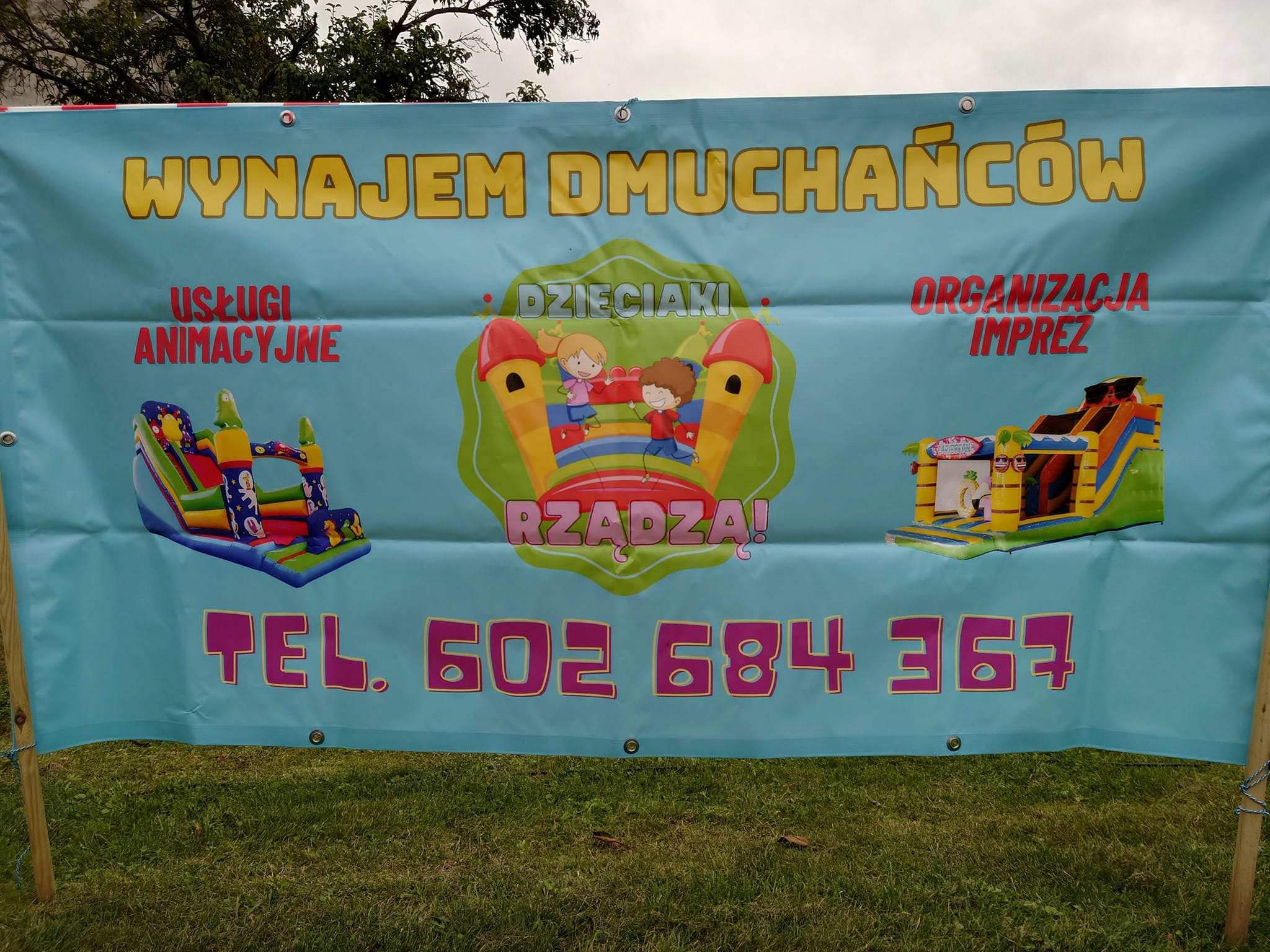 Baner reklamowy z napisem 'Wynajem dmuchańców' oraz informacjami o usługach animacyjnych i organizacji imprez dla dzieci, z ilustracjami dmuchanych zamków i numerem telefonu.