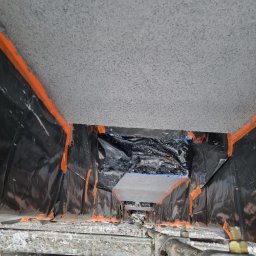 Adbud usługi ogólnobudowlane - Ocieplenie poddasza w trakcie realizacji, widok z rusztowania na folię ochronną, taśmę malarską i sufit po natrysku izolacji.