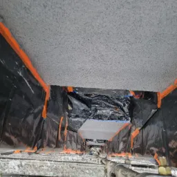 Ocieplenie poddasza w trakcie realizacji, widok z rusztowania na folię ochronną, taśmę malarską i sufit po natrysku izolacji.