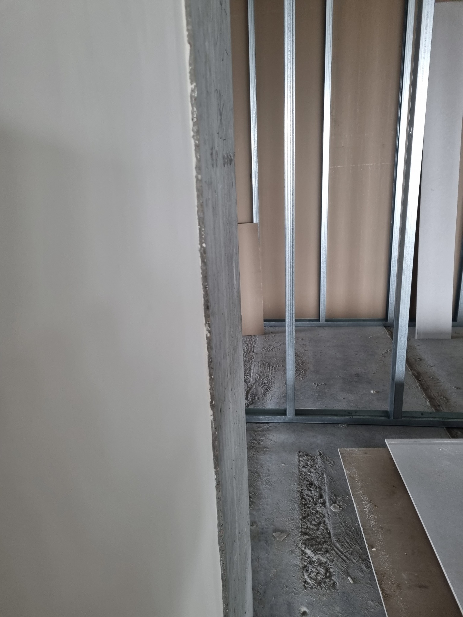 Wnętrze w trakcie prac wykończeniowych: konstrukcja szkieletowa z profili stalowych, częściowo obłożona płytami gipsowo-kartonowymi, surowy beton na ścianie z lewej strony, podłoże betonowe...