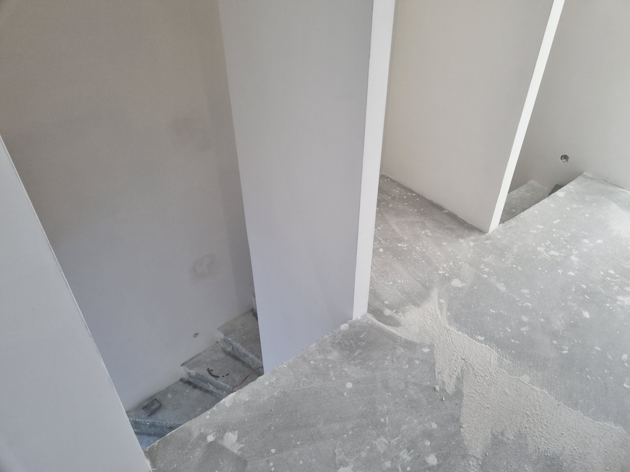 Wnętrze w trakcie malowania na biało, widoczne świeżo pomalowane ściany i surowy betonowy podkład z resztkami farby, przygotowywany do dalszych prac wykończeniowych.