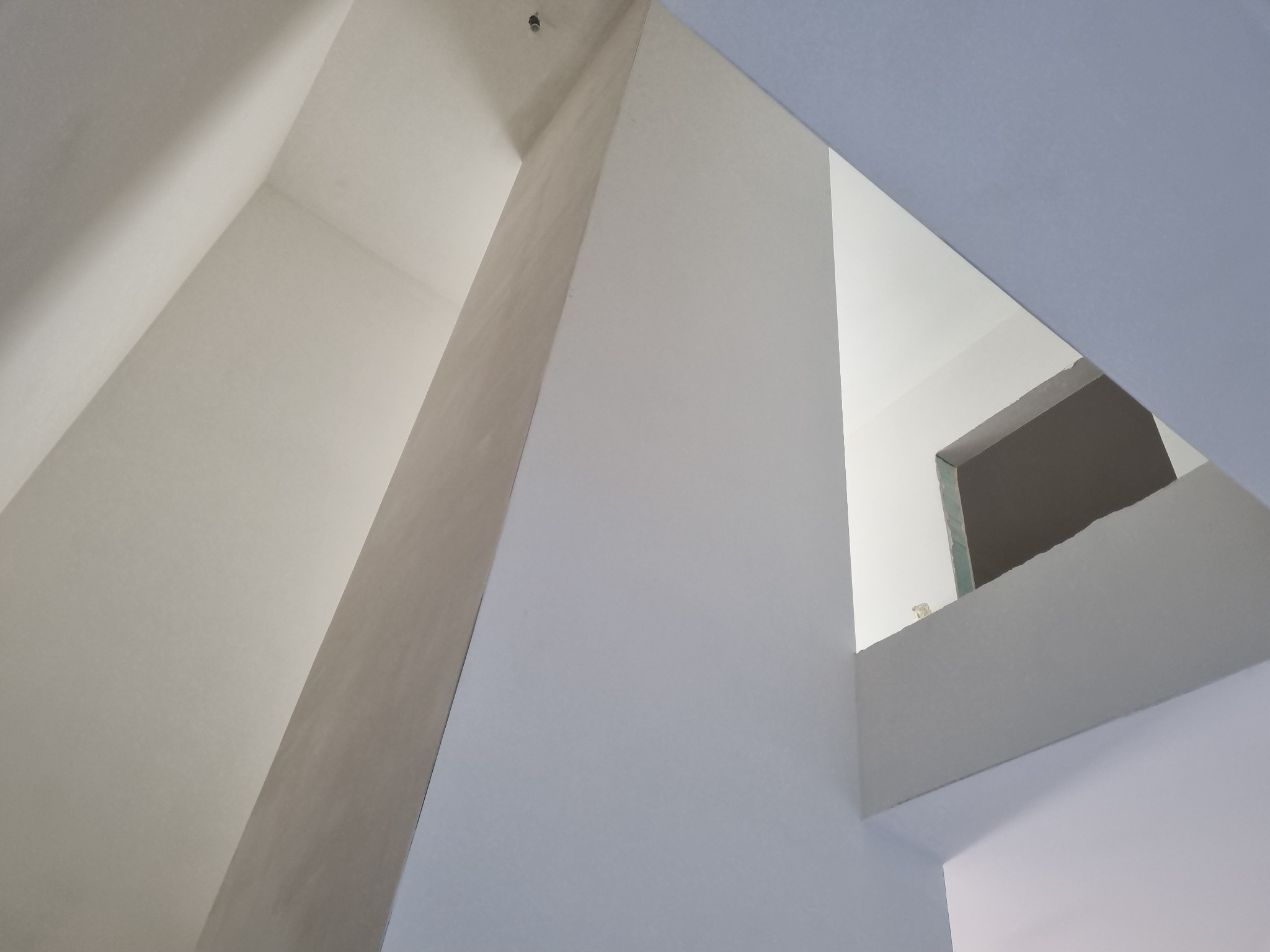 Wnętrze budynku w trakcie prac wykończeniowych, widok na sufit i ściany z nietypowym układem przestrzennym, widoczne łączenia płyt gipsowo-kartonowych i fragment otworu okiennego.