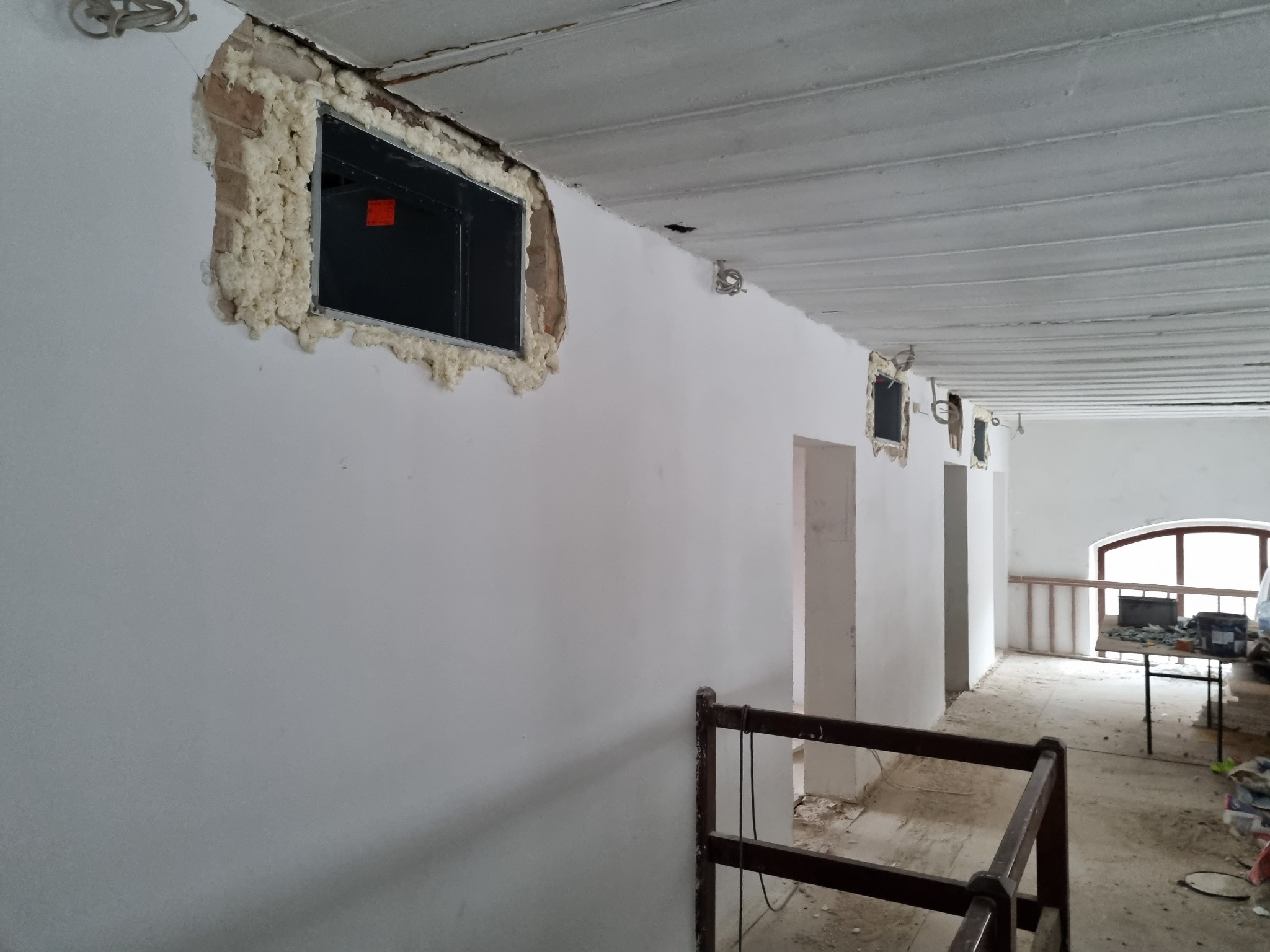 Wnętrze remontowanego poddasza z oknami w trakcie montażu, uszczelnionymi pianką montażową, widoczne drewniane belki stropowe i fragment balustrady.