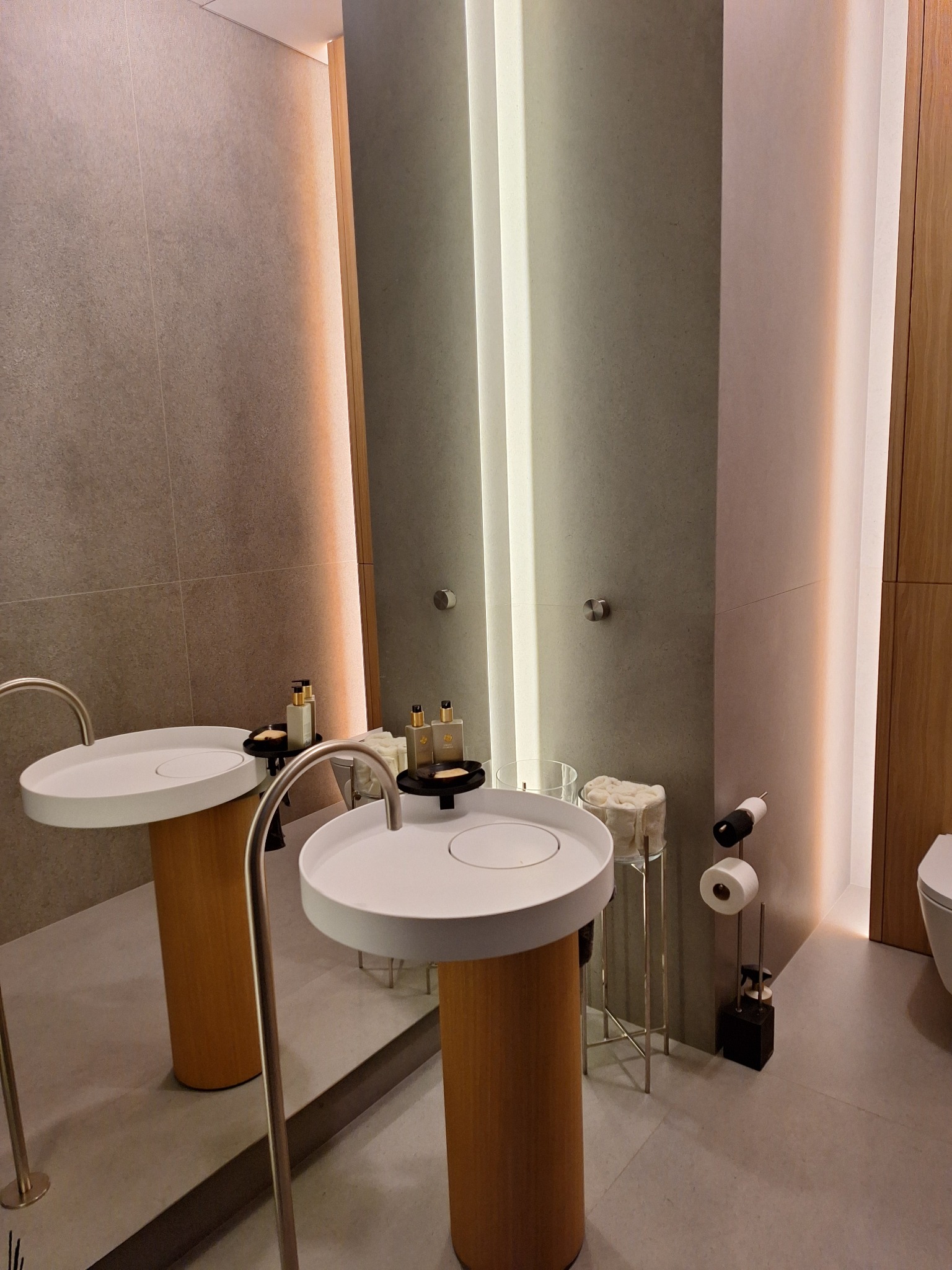 Nowoczesna łazienka z dwoma umywalkami na drewnianych postumentach, podświetlane lustro, minimalistyczny design, szara płytka ścienna, eleganckie akcesoria.