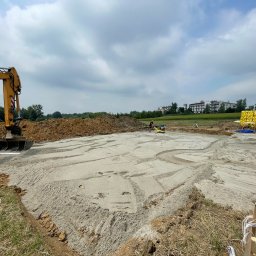FibroForm płyty fundamentowe - Żółta koparka Liebherr i pracownik wyrównujący piaszczyste podłoże pod konstrukcję, z widocznymi zwałami ziemi i żółtymi materiałami izolacyjnymi na placu budowy.
