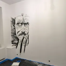 Wnętrze pokoju z białą ścianą ozdobioną czarno-białym, abstrakcyjnym rysunkiem portretowym. Na podłodze folia ochronna z resztkami farby i narzędziami malarskimi.