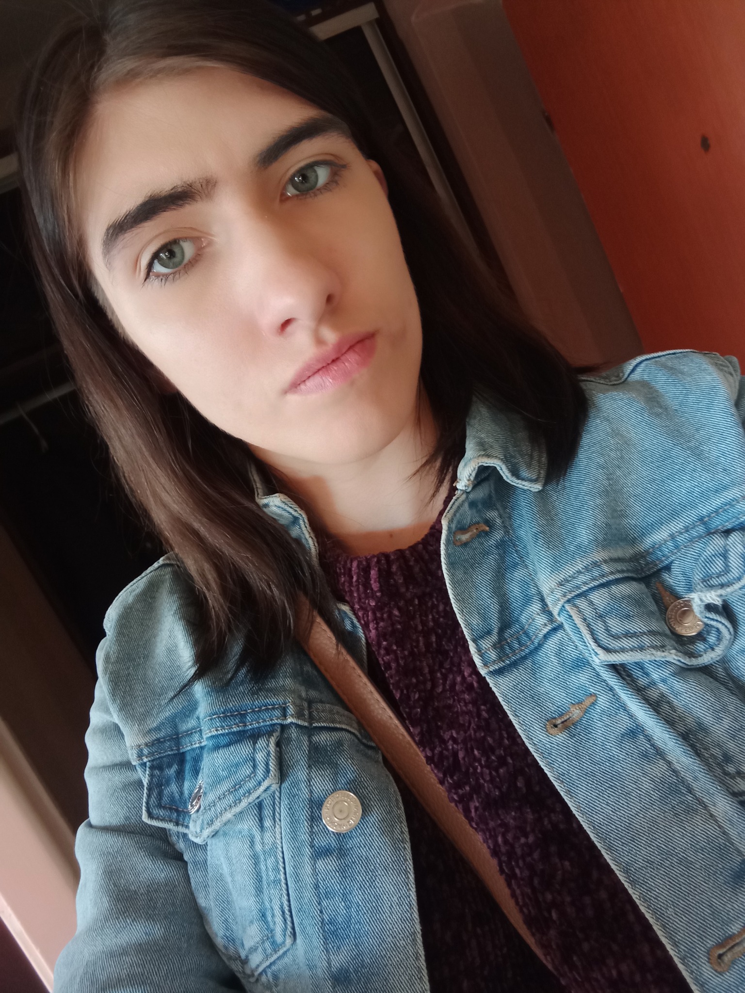 Portret młodej kobiety z zielonymi oczami, w dżinsowej kurtce i fioletowym swetrze, uchwycony pod kątem z bliska.