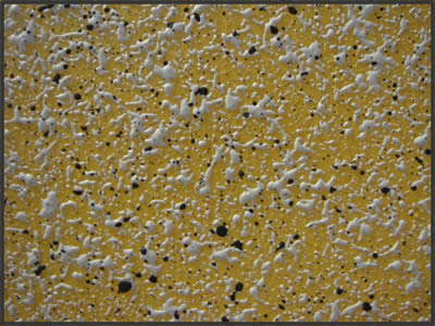 Żółta ściana pokryta dekoracyjnym tynkiem strukturalnym z białymi i czarnymi elementami.