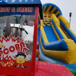 Automat do popcornu z napisem 'Hot & Fresh Popcorn' oraz dmuchana zjeżdżalnia z motywem Minionków w tle.