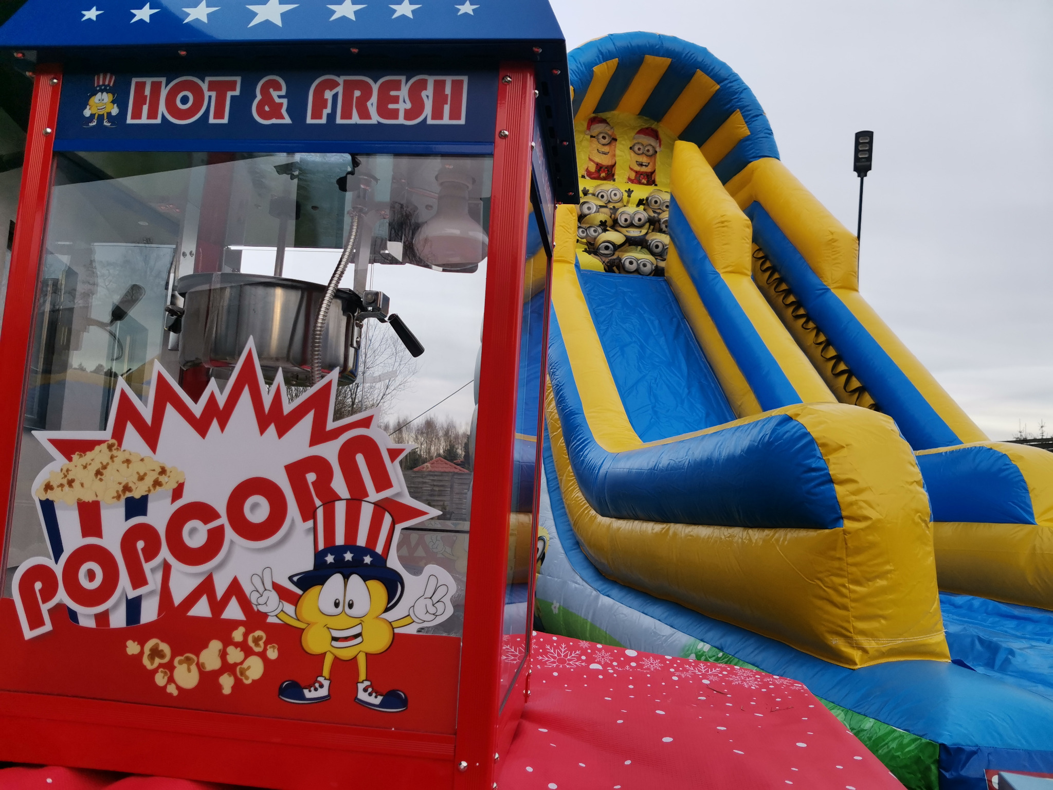 Automat do popcornu z napisem 'Hot & Fresh Popcorn' oraz dmuchana zjeżdżalnia z motywem Minionków w tle.