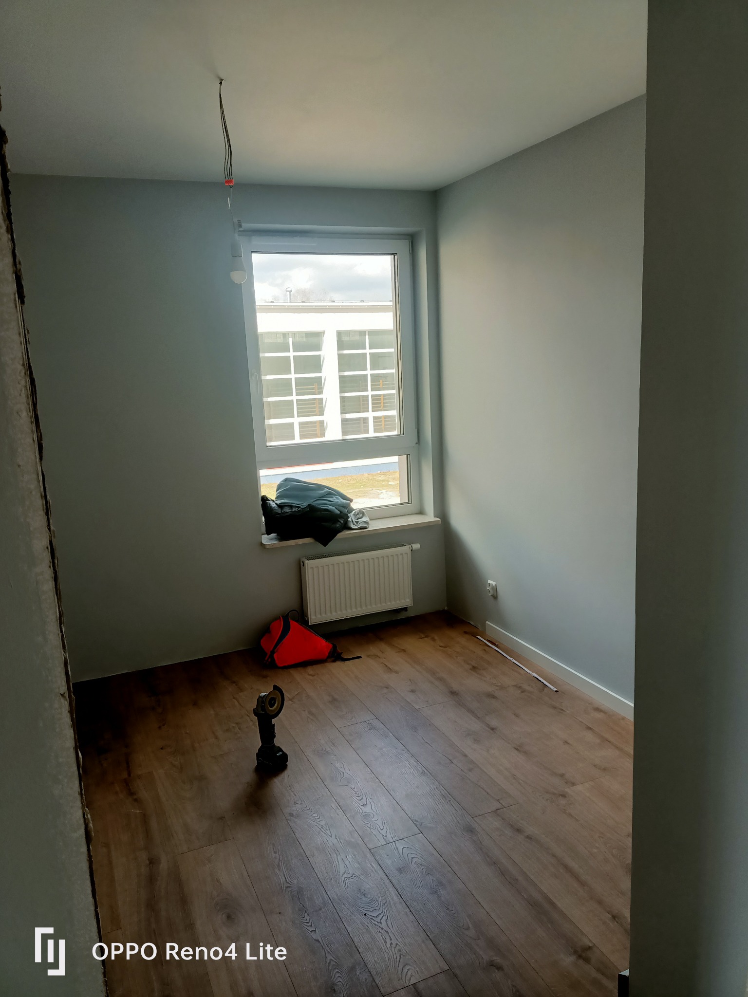 Pokój po remoncie z ułożonymi panelami podłogowymi, widoczna torba narzędziowa, włącznik światła i wystające kable z sufitu.