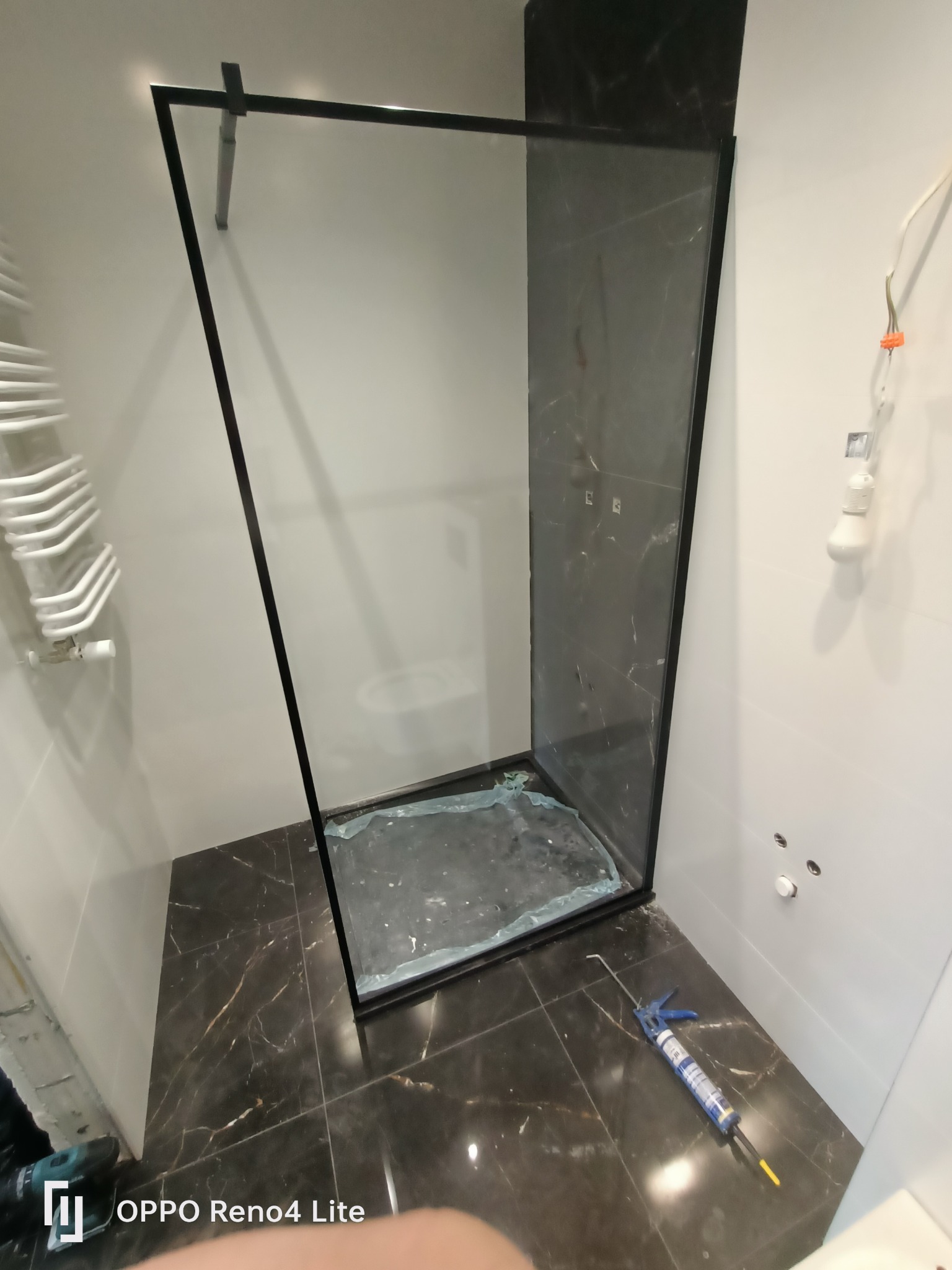 Montaż kabiny prysznicowej z czarnymi profilami i marmurowym wykończeniem w łazience w Białymstoku, widoczny silikon i narzędzia.