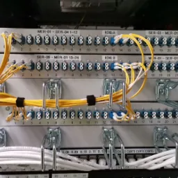 Panel krosowniczy z licznymi portami światłowodowymi, uporządkowane żółte i białe kable, metalowe uchwyty kablowe.