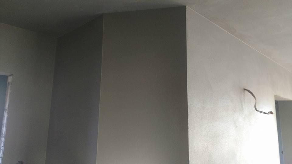 Świeżo nałożona, gładka, jasnoszara warstwa tynku na ścianie i suficie w rogu pokoju, z wystającym przewodem elektrycznym.