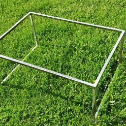 ParvisWelder Michał Gawarkiewicz - Surowa, spawana konstrukcja z metalowych profili w kształcie prostopadłościanu, umieszczona na trawniku z widocznymi białymi kwiatami.