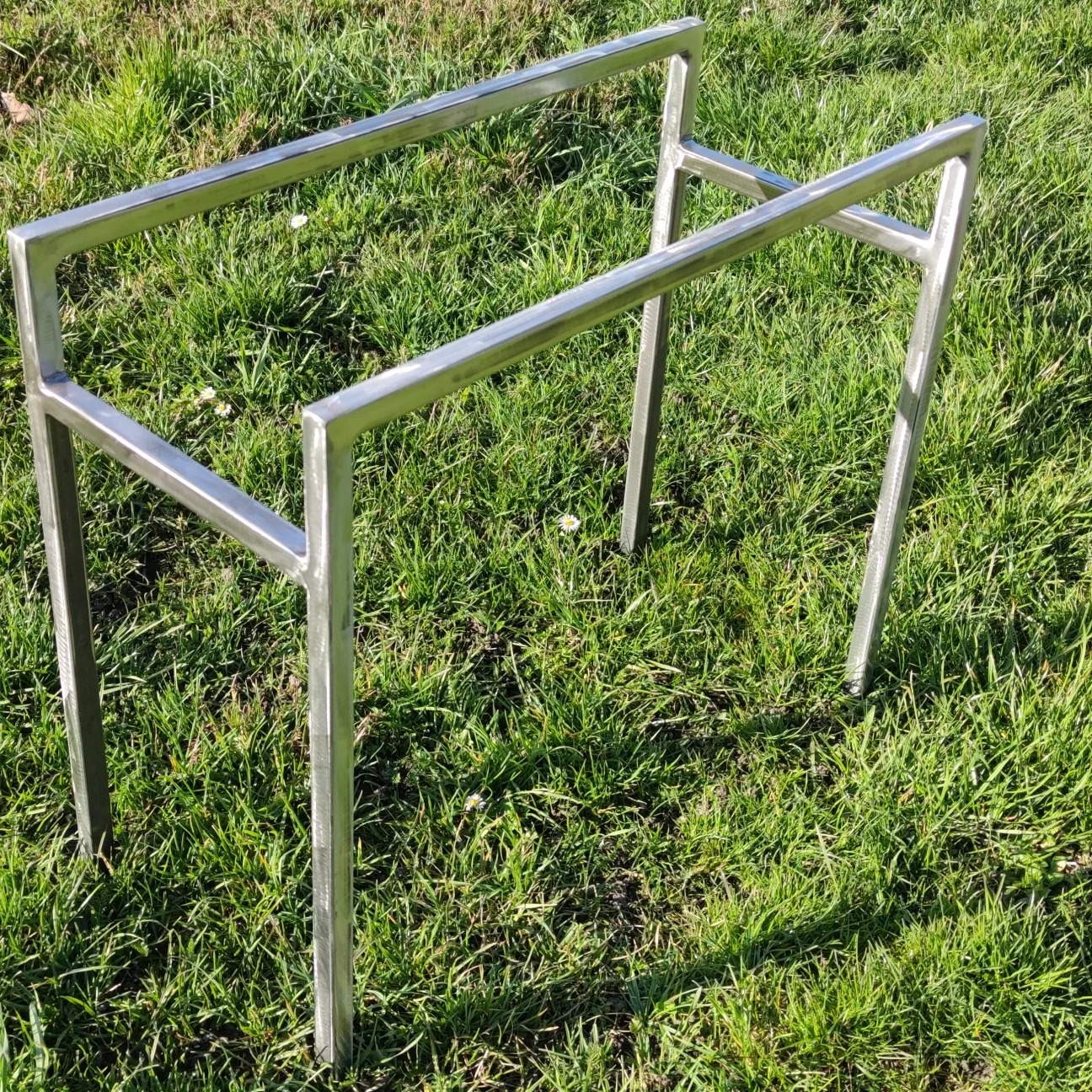 Surowa, metalowa konstrukcja schodów na trawie, widoczne spawy i niedoskonałości wykończenia.