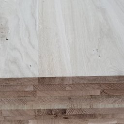 Wood Power Sp. z o. o. - Stos jasnych, klejonych desek drewnianych z widocznym przekrojem poprzecznym, ukazującym strukturę klejenia na tle szarej, betonowej podłogi.