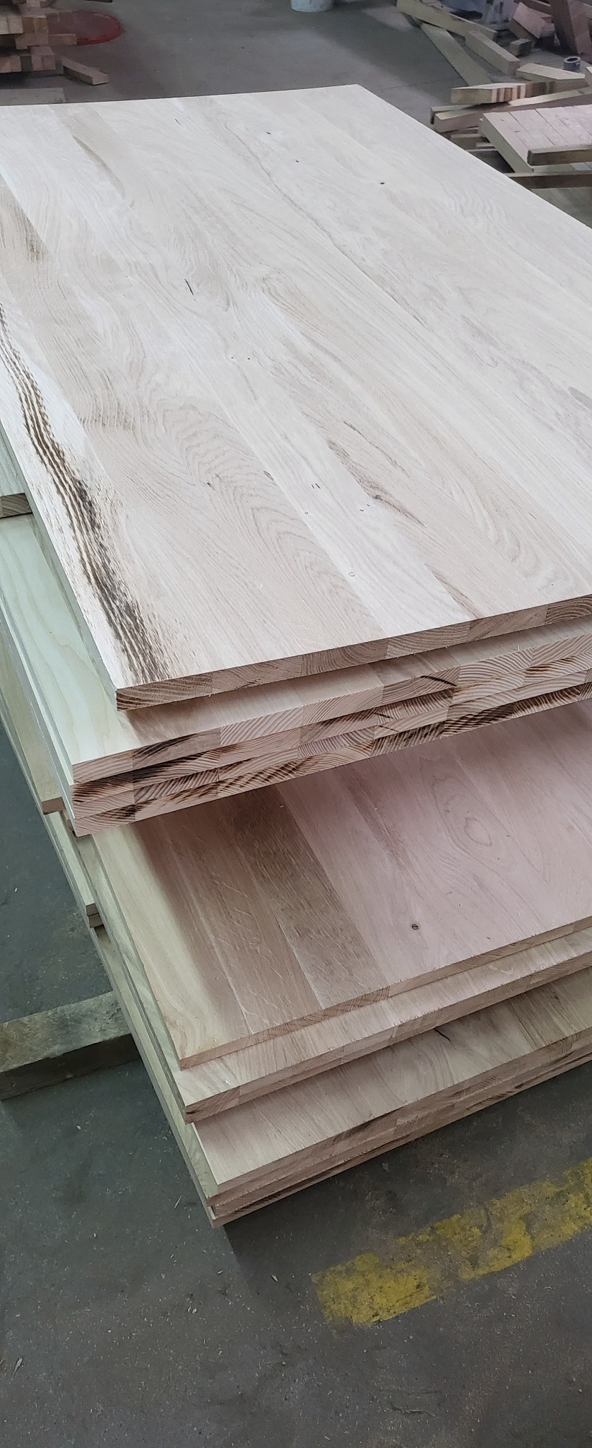 Stos jasnych, drewnianych płyt klejonych warstwowo, widoczne słoje drewna, przygotowanych do dalszej obróbki, leżących na palecie w hali produkcyjnej.