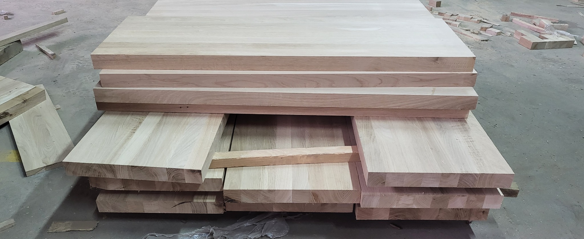 Stos jasnych, obrobionych desek z widocznymi słojami drewna ułożonych w magazynie lub warsztacie.