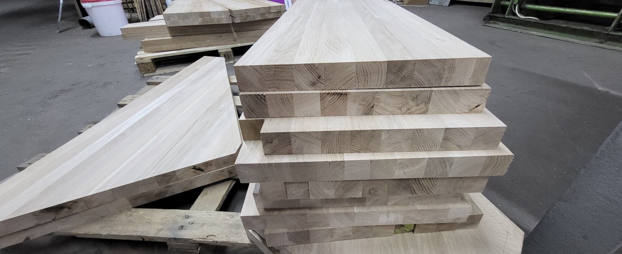 Stos ułożonych desek z klejonego drewna na paletach w hali produkcyjnej.