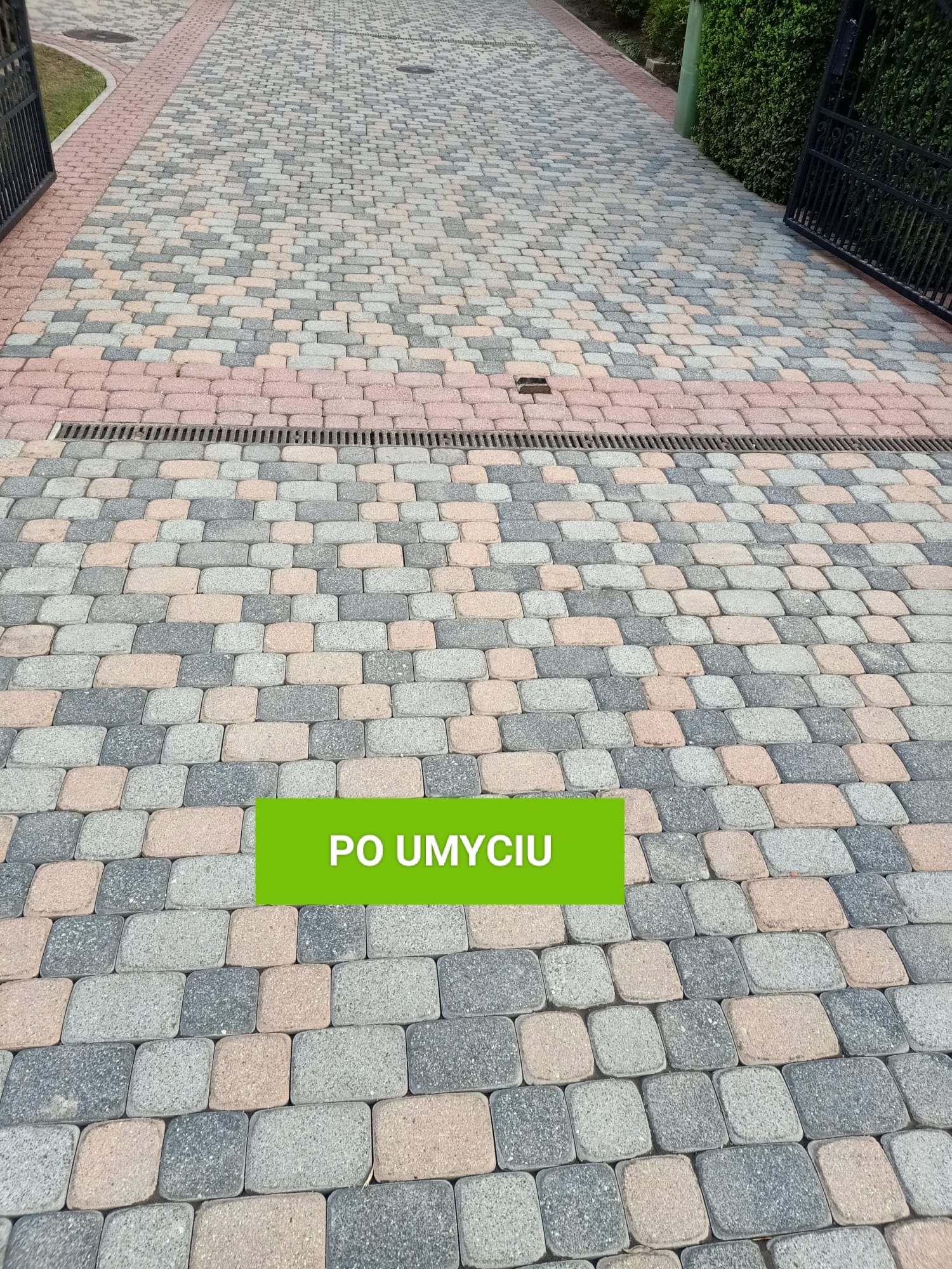 Wyczyszczona kostka brukowa w odcieniach szarości, brązu i różu, z widoczną kratką odpływową i otwartą bramą w tle.